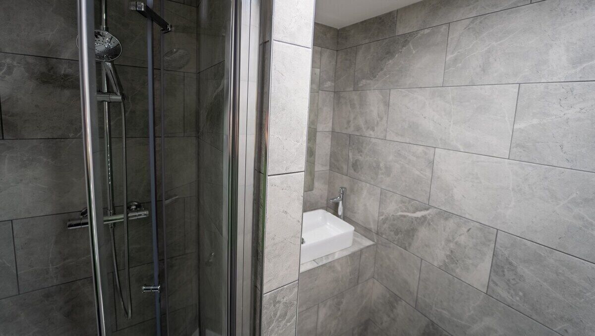 A modern bathroom with a glass-enclosed shower, a white sink, and grey tiled walls.