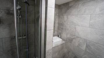 A modern bathroom with a glass-enclosed shower, a white sink, and grey tiled walls.