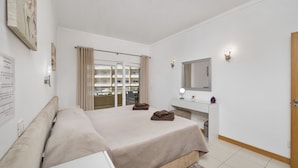 A hotel room with a large bed, a desk, a vanity with a mirror, and a view of a balcony with curtains. - Special Beachfront Sea View Apartment (Albufeira)