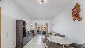 A modern living room with a dining area, a large window, and a view of a building. - Special Beachfront Sea View Apartment (Albufeira)