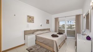A bedroom with a bed, bedside tables, a dresser, a mirror, and a view of the outside. - Special Beachfront Sea View Apartment (Albufeira)