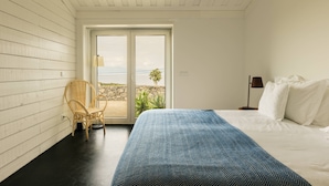Une chambre à coucher avec un lit, une chaise, une lampe et une vue sur l’extérieur, visible à travers une porte.