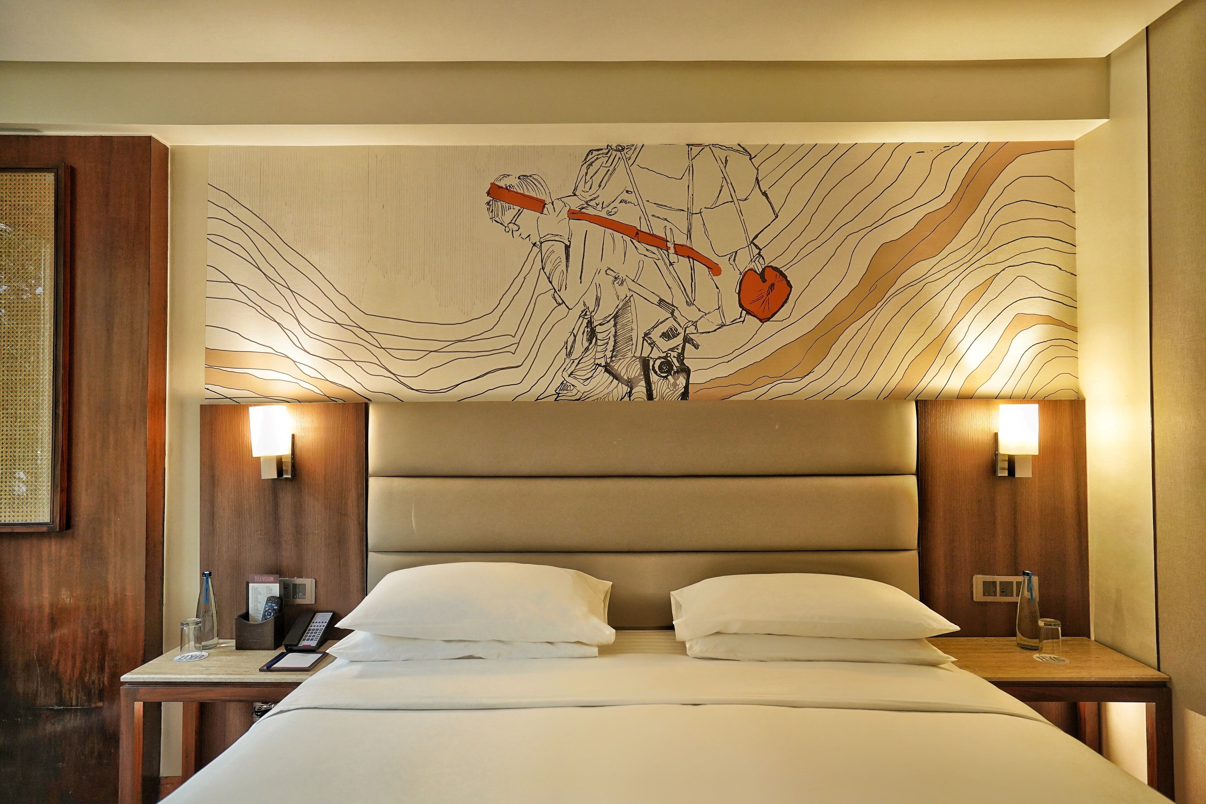 A hotel room with a large bed, two bedside tables, a headboard with a wall art piece, and two wall-mounted lamps.