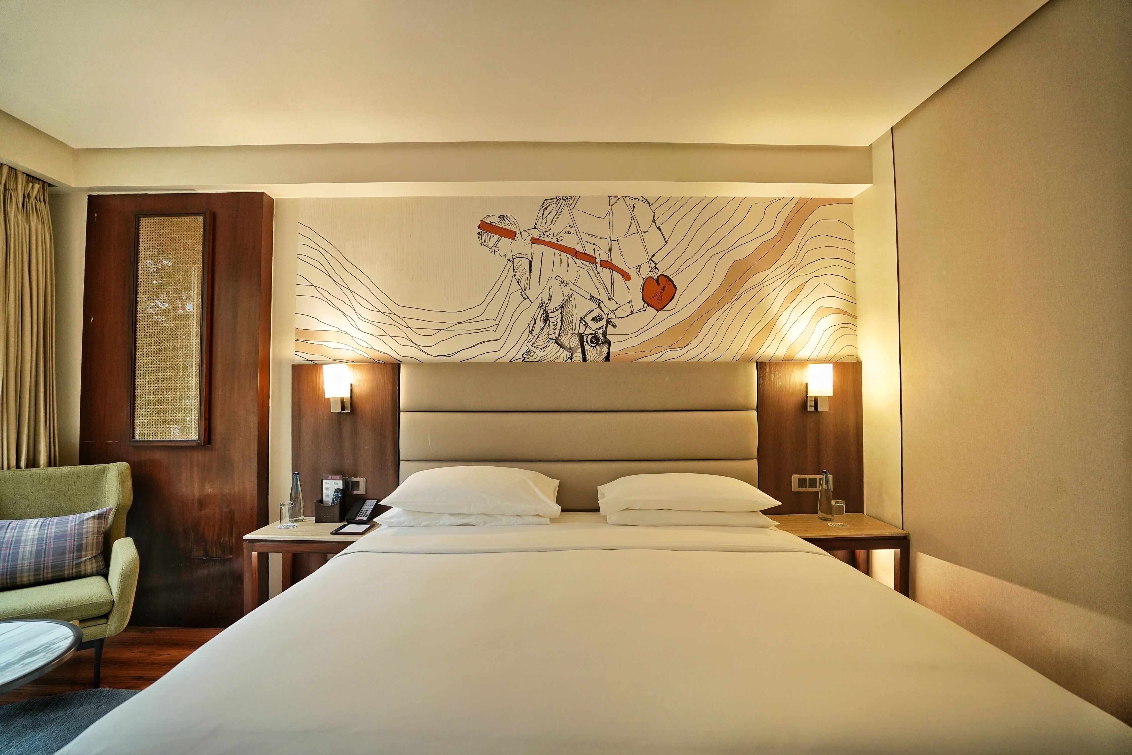 A hotel room with a large bed, two bedside tables, a nightstand, a chair, and a wall art piece.