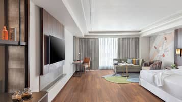 A modern hotel room with a large flat-screen TV, a sofa, a bed, and a dining area.