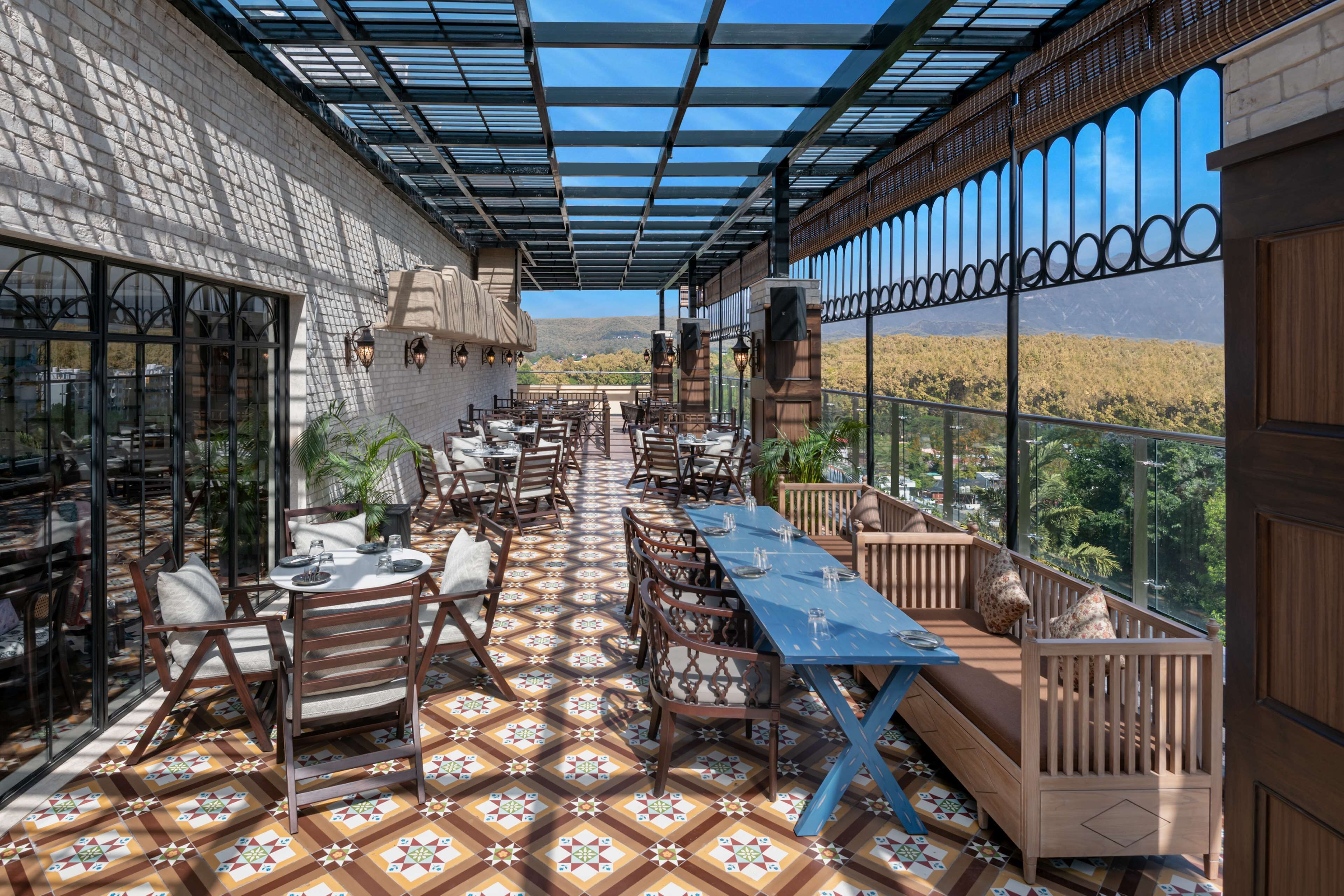 Un patio al aire libre con piso estampado, mesas, sillas y vista a un paisaje montañoso.