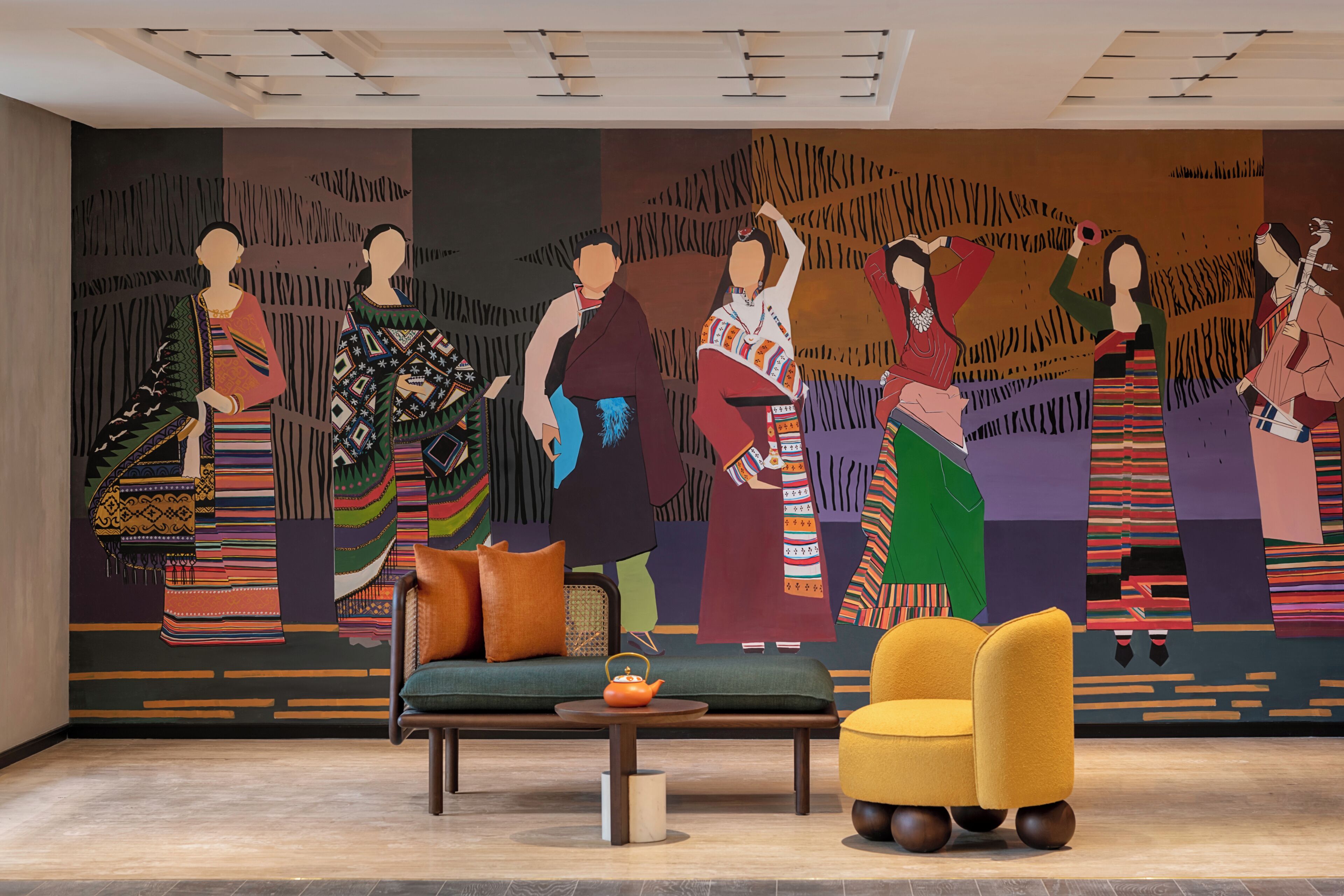 A modern interior with a mural of indigenous people, a sofa, a yellow armchair, and a small table with a teapot.