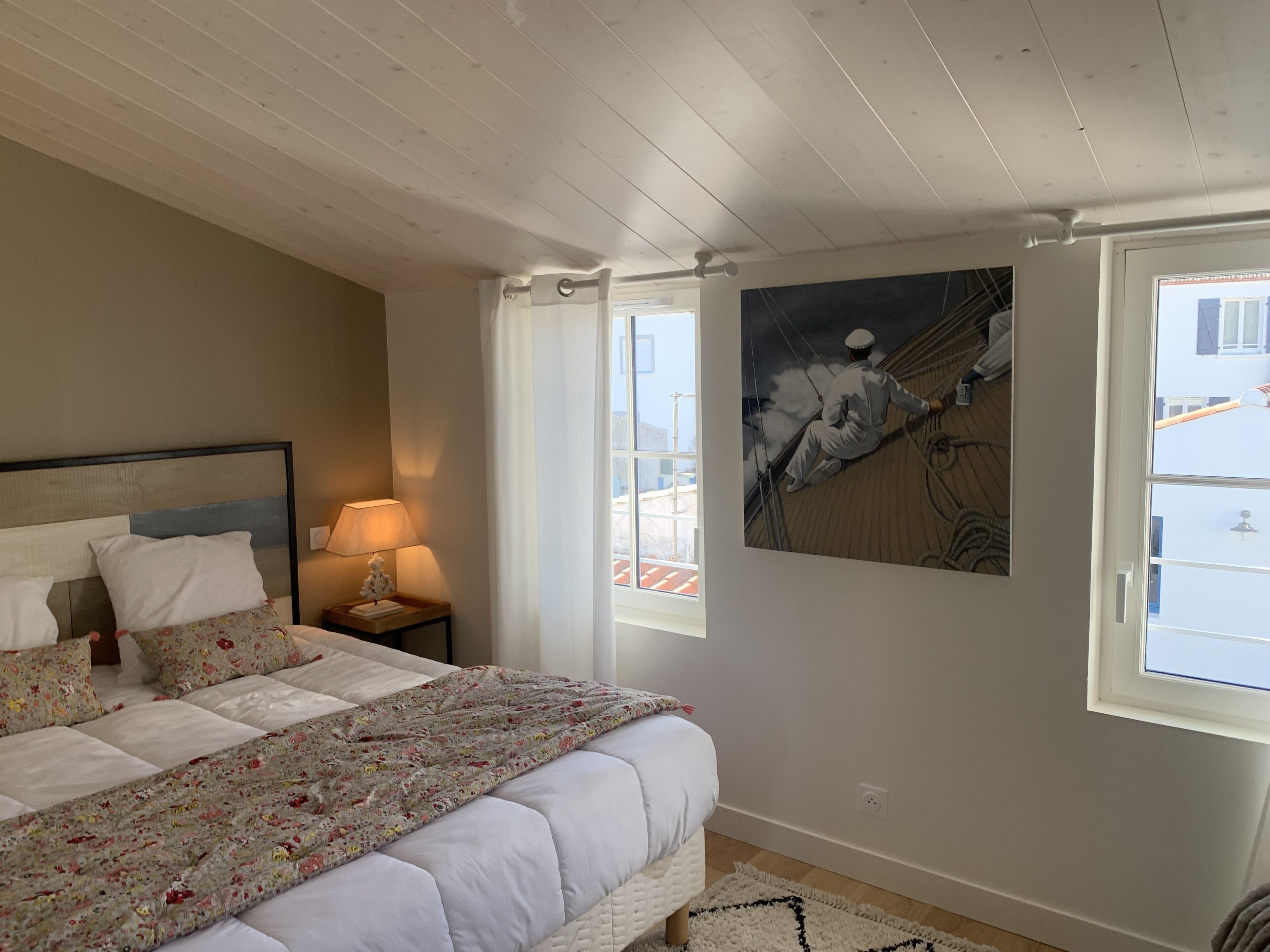 Un dormitorio con cama, una mesita de noche, una lámpara, una ventana con cortinas y un cuadro en la pared.