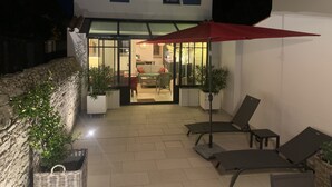 Una casa de dos pisos con un patio que tiene mobiliario exterior y un paraguas rojo.