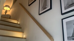 Una escalera de madera con barandilla, que lleva a un rellano con cuadros de veleros en la pared.
