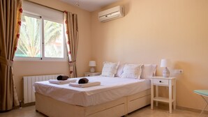 Ein Schlafzimmer mit einem Bett, zwei Nachttischen, einer Ablage, einem Fenster mit Vorhängen, einer Klimaanlage und einer Heizung.