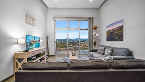 A modern living room with a large sofa, a television, and a scenic view through a large window. -  Casa Buena Vista (Valle de Guadalupe)
