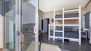 A modern bedroom with bunk beds, a glass door leading to a balcony, and a view of the countryside. - Casa Buena Vista (Valle de Guadalupe)