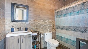 Een badkamer met een houten vloer, een wastafel met spiegel, een toilet en een douchegordijn met een patroon.