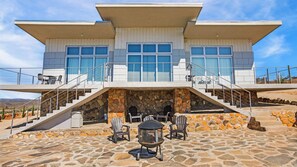 A modern two-story house with a stone facade, outdoor seating area, and a staircase leading to a balcony. - Casa Buena Vista (Valle de Guadalupe)
