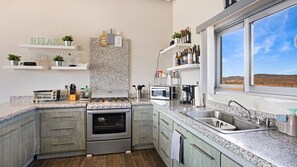 A modern kitchen with granite countertops, a built-in stove, and a window with a view of the desert. - Casa Buena Vista (Valle de Guadalupe)