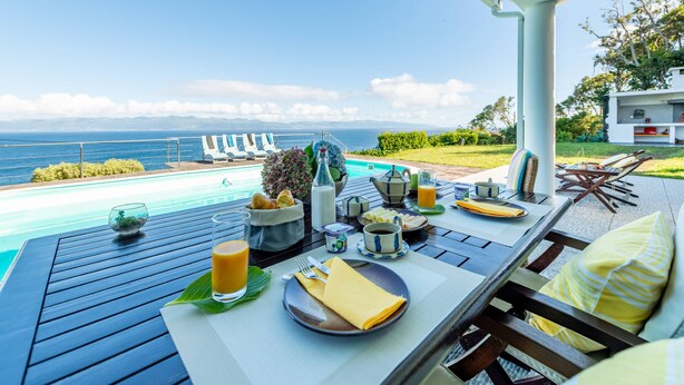 Una mesa de comedor con alimentos para el desayuno, vistas al mar y mobiliario exterior.