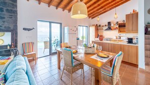 Amplia sala de estar con techo de madera, una mesa de comedor lista para cuatro comensales y una cocina con armarios de madera.