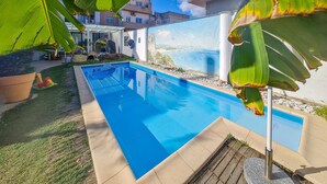 Une piscine à l’eau d’un bleu limpide, entourée d’une terrasse en béton et d’une zone herbeuse.
