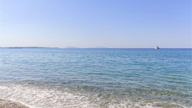 Une vue dégagée sur une mer calme, avec un navire au loin et un ciel clair.