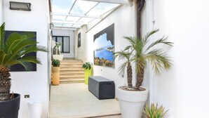 Un couloir étroit avec un escalier menant à une porte, de part et d’autre duquel se trouvent des plantes en pot et des tableaux encadrés accrochés aux murs.