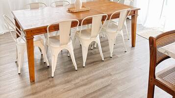 Un comedor con una mesa de madera y sillas blancas, una lámpara colgante de fibra y una planta en maceta.