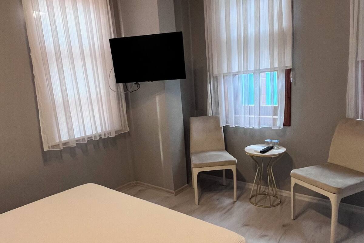 A hotel room with a bed, two chairs, a small table, and a TV mounted on the wall.