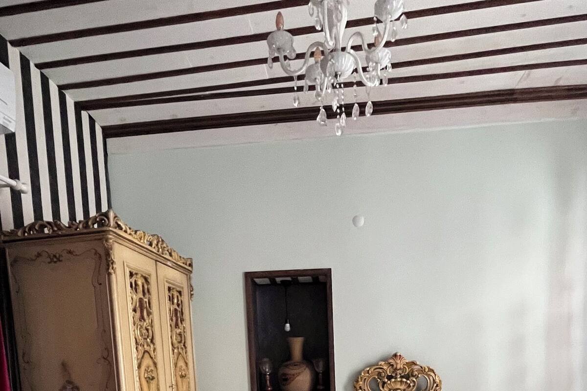 A bedroom with a large ornate bed, a chandelier, a cabinet, and a framed picture on the wall.