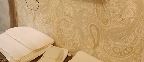 Una habitación con una televisión de pantalla plana en la pared, un papel tapiz estampado y una pila de toallas blancas sobre un banco de madera.