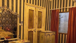 A room with striped wallpaper, a bed with rose petals and a balloon, a desk with a mirror, and a wardrobe. - Mazi Otel (Mudanya)
