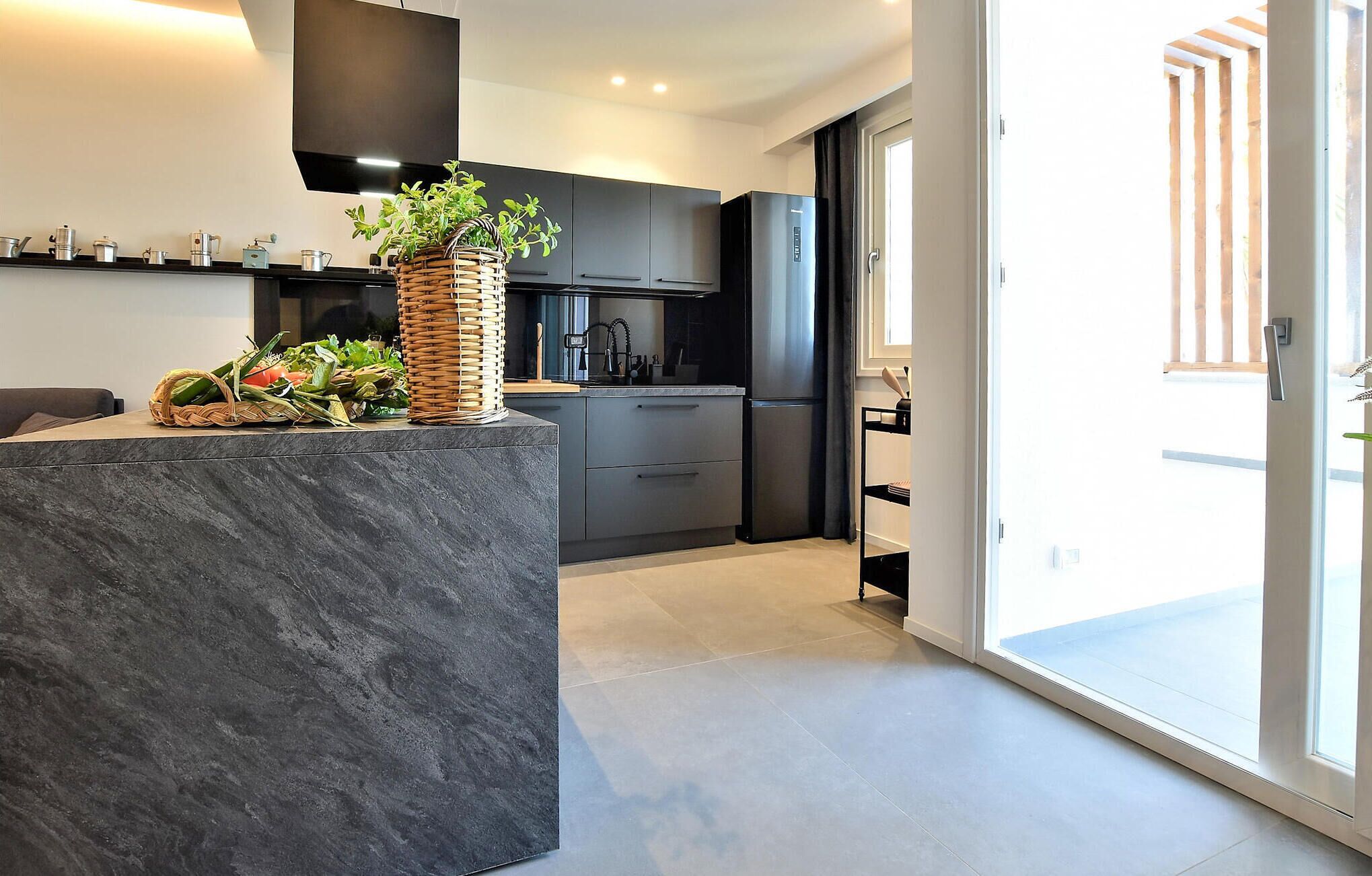 Une cuisine moderne avec des meubles de couleur sombre, un plan de travail en marbre et un panier en osier rempli de produits frais.
