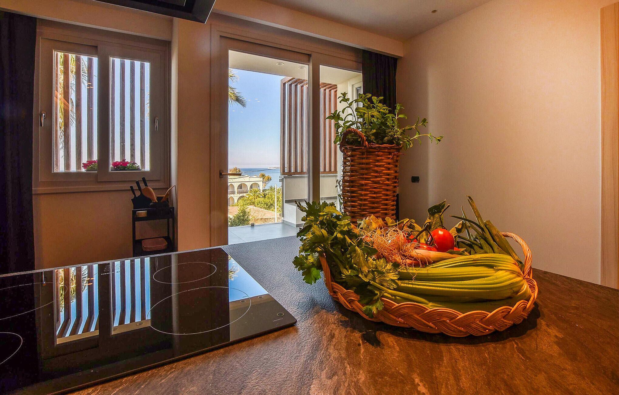 Une chambre d’hôtel moderne avec une grande fenêtre, une table à manger agrémentée d’un panier de produits frais et une chaise.