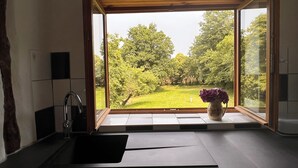 A kitchen with a large window, a sink, and a vase with flowers. - A tastefully renovated farmhouse in the tranquil la Creuse department of France. (Fursac)