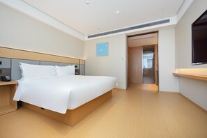 A modern hotel room with a large bed, bedside tables, a desk, and a flat-screen TV.