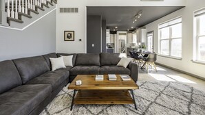 Una sala de estar moderna con un sofá seccional de cuero oscuro, una mesa de centro de madera y una escalera con barandillas blancas.