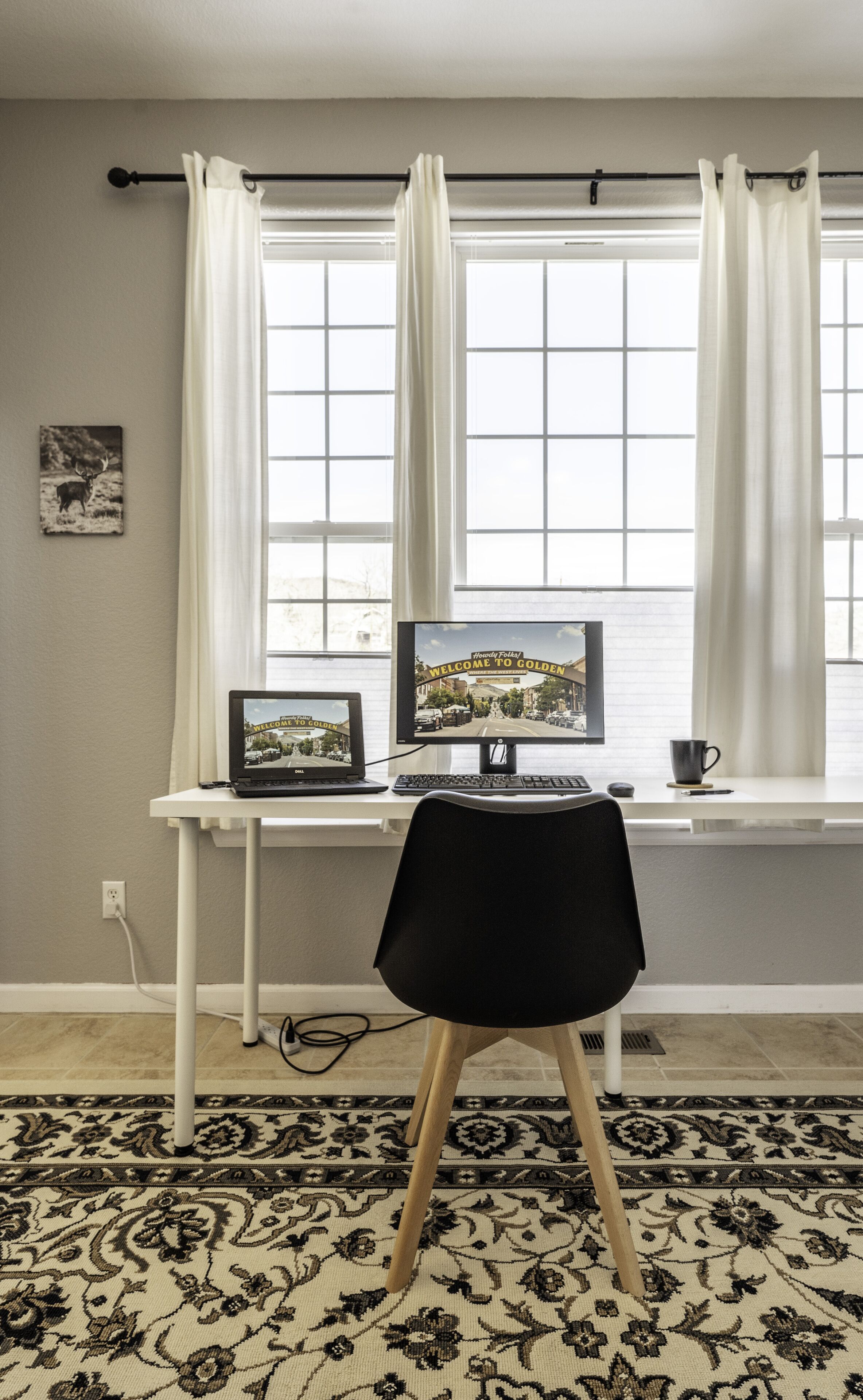 A workspace with a computer, a chair, a rug, and a window with curtains.