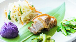 Ein Teller mit verschiedenen Speisen, darunter eine violette Knödel, ein Fleischstück und Gemüse.