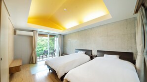 Ein Hotelzimmer mit zwei Betten, einem Balkon mit Blick auf Grünflächen, einer Deckenleuchte und einer Betonwand.