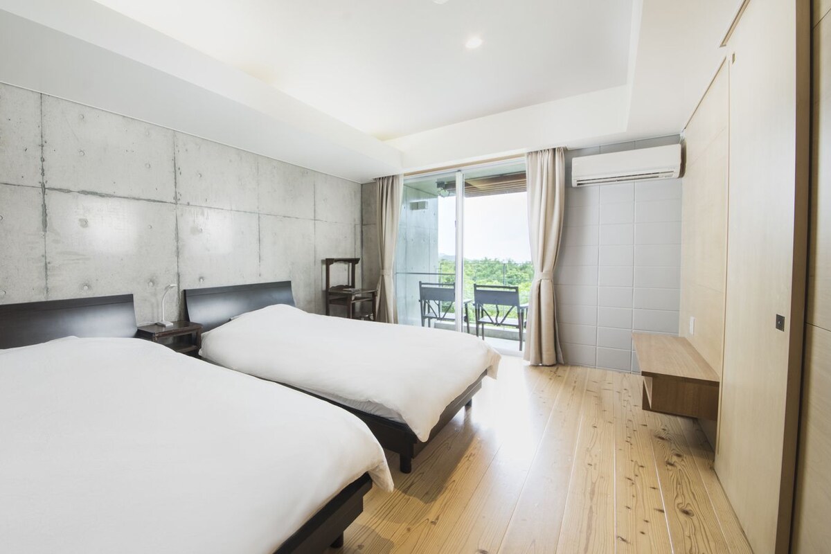 Habitación de hotel moderna con dos camas, un balcón con vistas y suelo de madera.