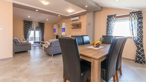 A modern dining area with a wooden table, black leather chairs, and a fruit bowl. There is a sofa and a TV in the background. - Beautiful home in Ceranje Gornje (Ceranje Gornje)