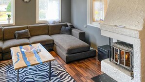 Een woonkamer met een hoekbank, een houten salontafel, een open haard en een vloerkleed met zebraprint.