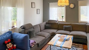 Een woonkamer met een hoekbank, een blauwe fauteuil met een zacht knuffeldiertje, een houten salontafel en een vloerkleed met zebraprint.