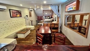 Hotelkamer met een bed, een bank, een eettafel, stoelen, een spiegel en een plafondventilator.