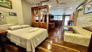Een hotelkamer met een bed, een houten garderobe, een eethoek en een zithoek.