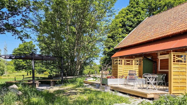A wooden cabin with a tiled roof, a patio with outdoor furniture, and a pergola structure. - Nice apartment in Vedum with WiFi (Vedum)