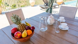 Una mesa de madera con un frutero, una jarra, tetera, tazas y vasos.