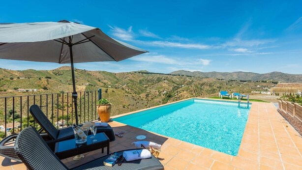 Zona de piscina con vistas a las colinas, una mesa con bebidas y sillones de descanso.