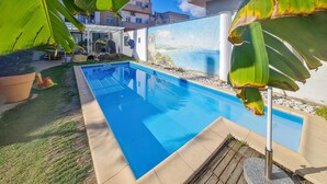 Una piscina rectangular amb aigua blava cristal·lina, envoltada per un solàrium de formigó i una zona verda.