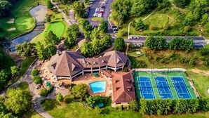 Vue aérienne d’un terrain de golf avec un club-house, des courts de tennis et une piscine.