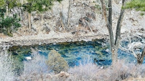 Un paisaje natural con un arroyo cristalino, terreno rocoso y vegetación escasa.